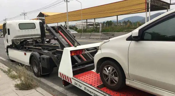 Pomoc drogowa w akcji: białe auto jest ładowane na lawetę. Widać, jak holować auto, gdy jest potrzebna pomoc.