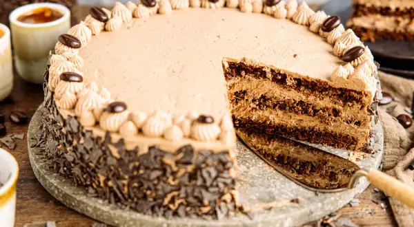 Eine köstliche Kaffee Torte mit Schokoladenraspeln und Kaffeebohnen-Dekoration. Ein Stück wurde bereits angeschnitten.