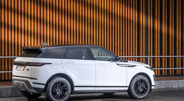 Weißer Range Rover Evoque Benziner mit schwarzem Dach parkt vor einer Holzwand.