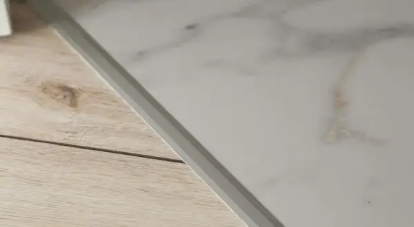Un battiscopa in laminato effetto metallo separa un pavimento in finto marmo da uno in finto legno.