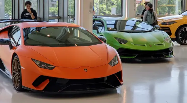 Pomarańczowy i zielony Lamborghini w muzeum Lamborghini. Obok żółty SUV.