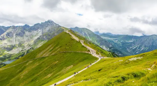 Tłum ludzi wędruje malowniczymi szlakami górskimi w Polsce, podziwiając skaliste szczyty i zielone zbocza.