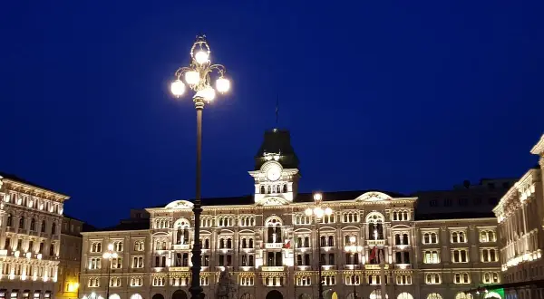 Piazza Unità d'Italia a Trieste, illuminata di sera. Edifici storici e lampioni creano un'atmosfera magica.
