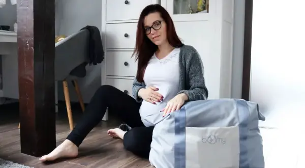 Przyszła mama przygotowuje listę rzeczy do szpitala, siedząc obok torby.