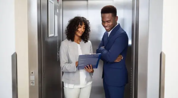 Zwei Geschäftsleute im Aufzug, die Notizen besprechen. Ein kurzer elevator pitch, bevor die Türen sich öffnen.