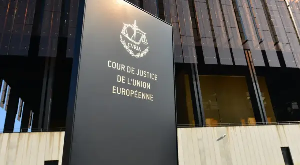 Tablica z napisem "Cour de Justice de l'Union Européenne" przed nowoczesnym budynkiem. To siedziba Trybunału Sprawiedliwości Unii Europejskiej.