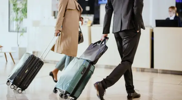 Biznesmeni z walizkami w hotelowym lobby, gotowi na polecenie wyjazdu służbowego.