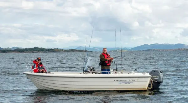 Zwei Männer genießen das Angeln in Norwegen auf einem Boot. Eine Möwe schwimmt im Wasser.