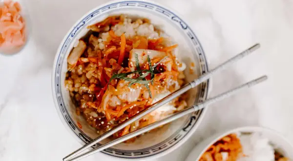 Miseczka z ryżem i pikantnym, fermentowanym kimchi, ozdobiona szczypiorkiem. Pałeczki czekają, by spróbować tego koreańskiego przysmaku.