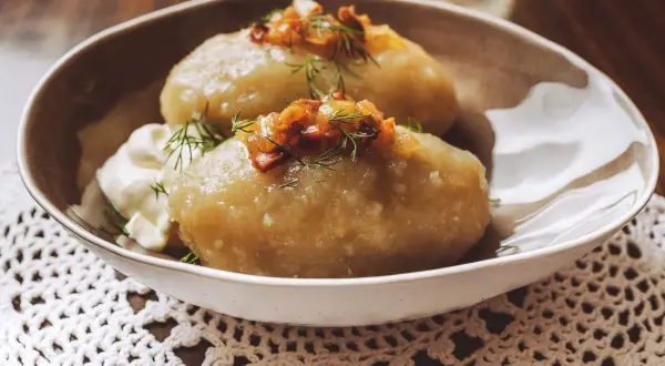 Cepelinai, comida típica de Lituania, servidos con crema agria y tocino crujiente.