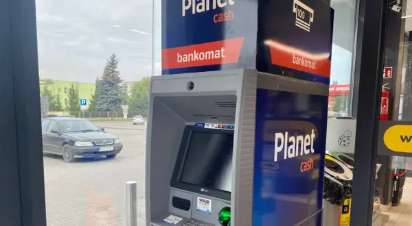 Bankomat Santander Planet Cash przy parkingu. Obok stoi czarny samochód.