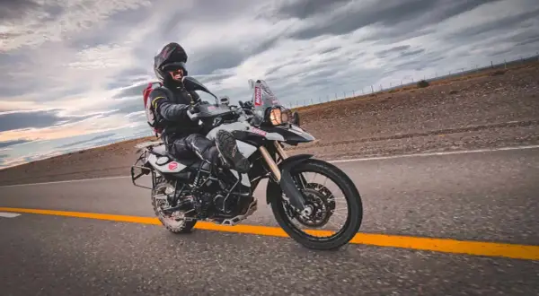 Motocyklista w kasku i kurtce pędzi na motocyklu BMW F 800 po pustej drodze pod burzowym niebem.
