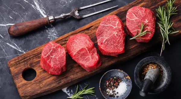 Mięso wołowe na desce, idealne na dietę dla grupy krwi 0. Obok przyprawy i rozmaryn.