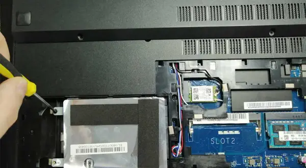 Ręka przykręca śrubkę mocującą dysk SSD w laptopie. Poradnik: jak zamontować dysk SSD.