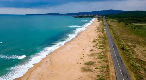 Bułgaria jakie morze? Piękna, turkusowa woda obmywa piaszczystą plażę, a w oddali widać zabudowania i zielone wzgórza. Droga wzdłuż wybrzeża zaprasza do podróży.