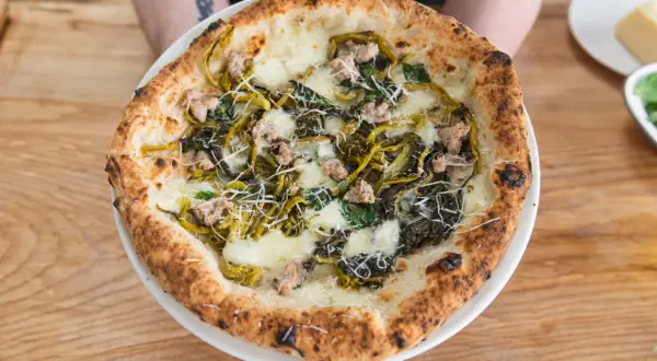 Pizza mit Salsiccia und Friarielli, belegt mit geschmolzenem Käse und geriebenem Parmesan.