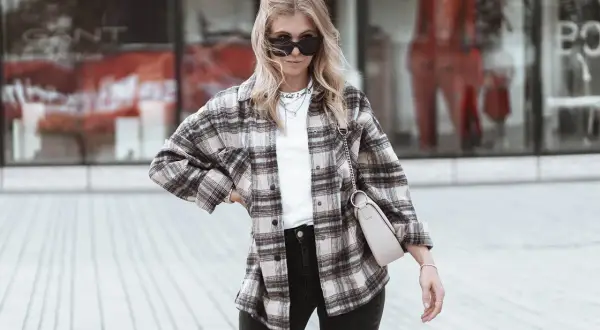 Frau im lässigen Flanellhemd-Style mit Sonnenbrille und Tasche.