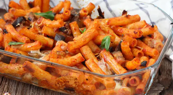 Piatto fumante di pasta alla siciliana in teglia, con melanzane, pomodoro e formaggio filante.