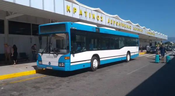 Niebiesko-biały autobus na Korfu, symbol komunikacji miejskiej, czeka na pasażerów przed budynkiem lotniska.