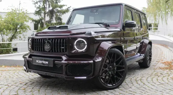 Mocarny Brabus 700 w bordowym kolorze, z czarnymi felgami i charakterystycznym grillem, prezentuje się imponująco na brukowanej nawierzchni.