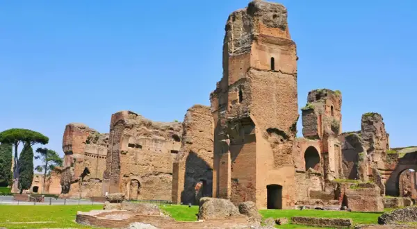 Imponenti rovine delle terme di Caracalla a Roma, con torri di mattoni che si ergono contro il cielo azzurro.