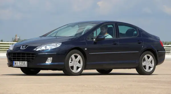 Ciemnoniebieski Peugeot 407 z widocznymi żarówkami reflektorów, kierowca za kierownicą.