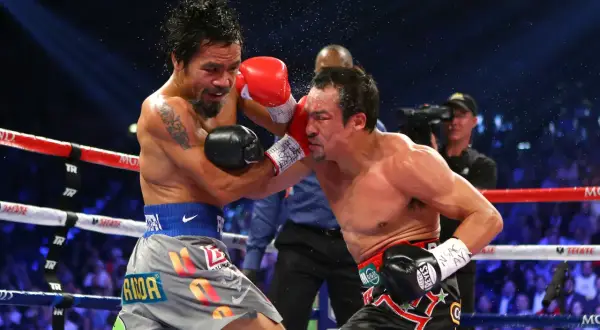 Manny Pacquiao lands a punch on Juan Manuel Marquez during their intense boxing match. Sweat flies as the crowd roars.
