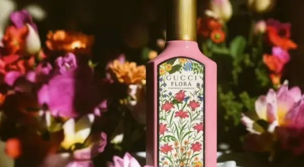 Różowa butelka Gucci Flora Gorgeous Gardenia 100ml otoczona bujnymi, kolorowymi kwiatami.