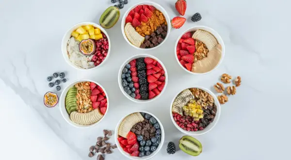 Sju skålar med färgglada frukter, granola och nötter. Perfekta för nyttiga snacks recept som ger energi.