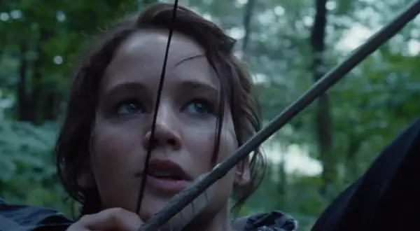 Katniss Everdeen spänner sin båge i skogen, redo för kampen i hunger games filmserie.