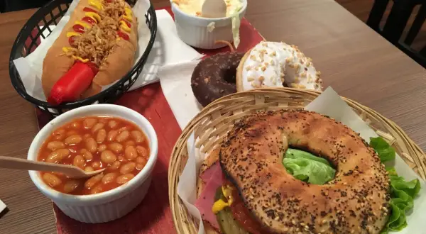 Un bagel de l'ouest garni de viande, salade et cornichons, accompagné d'un hot-dog, de haricots à la tomate, de salade de chou et de deux donuts.