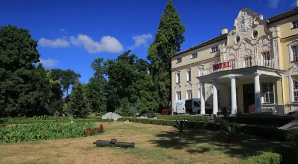 Pałac w Witaszycach, dawniej hotel, otoczony zielenią. Na trawniku leży zabytkowa armata.