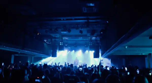 Tłum na koncercie lil tracy, ludzie nagrywają telefonami, światła sceniczne tworzą niebieską poświatę.