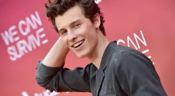 Uśmiechnięty Shawn Mendes na tle napisu "We Can Survive". Czeka na swój **shawn mendes koncert**.