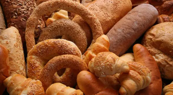 Różnorodne rodzaje chleba i bułek, w tym bochenki z ziarnami, precle z sezamem i rogaliki, tworzą apetyczną kompozycję.
