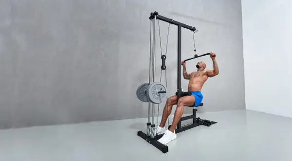 Man tränar latsdrag muskler på ett gym. Han sitter på en bänk och drar ner en stång med vikter.