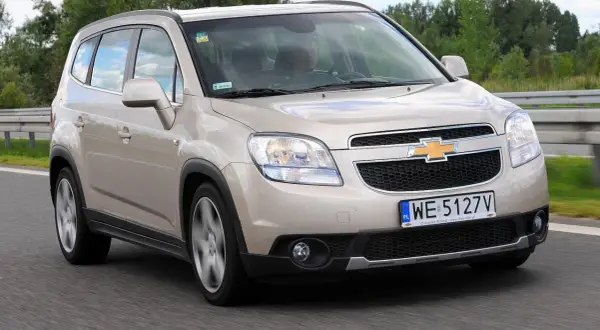 Złoty Chevrolet Orlando 1.8 benzyna na drodze. Rodzinny minivan w ruchu, z widocznym kierowcą.