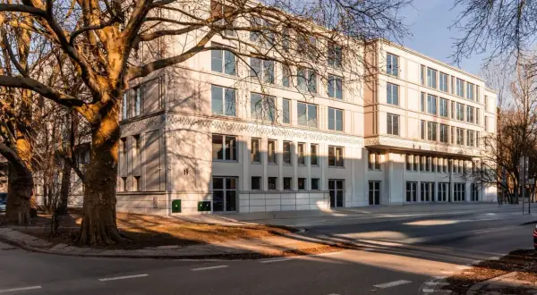 Nowoczesny budynek mieszkalny z dużymi oknami i drzewami w pobliżu, w słoneczny dzień.