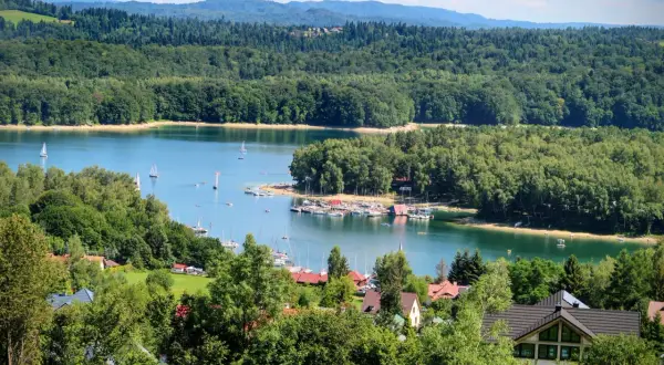 Malowniczy widok na Jezioro Solińskie z żaglówkami i lasami. Idealne miejsce, by sprawdzić, jak dojechać nad Solinę samochodem i odpocząć.