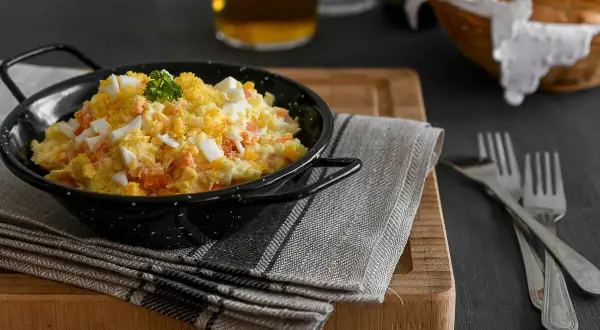 Una deliciosa ensalada rusa, cremosa y con trozos de huevo duro y zanahoria, servida en un cuenco negro.