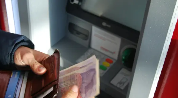 Ręce trzymają portfel z kartami i banknotami przy bankomacie. Sprawdzam stan konta bankowego.