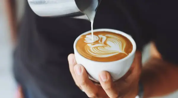 Un barista crea un disegno a cuore con latte per cappuccino su un caffè.
