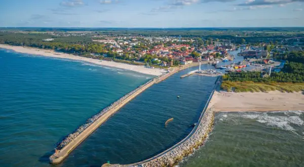Widok z lotu ptaka na port w Ustce z falochronami, plażą i miastem w tle.
