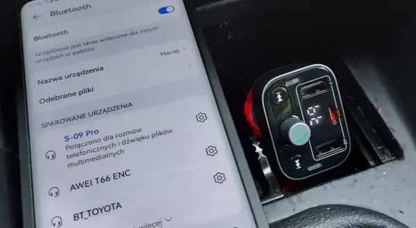 Jak ustawić transmiter w aucie? Na ekranie telefonu widać menu Bluetooth, a obok transmiter samochodowy podłączony do gniazda zapalniczki.