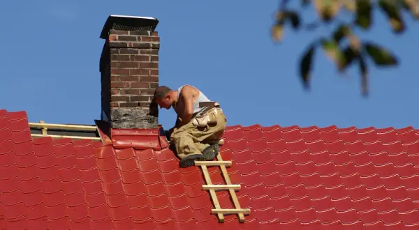 Handwerker dichtet den Schornstein am roten Ziegeldach ab.