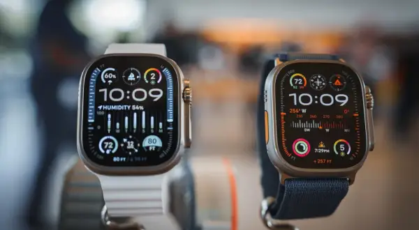 Deux montres connectées Apple, l'une avec bracelet blanc, l'autre bleu, affichent l'heure et des données météo.