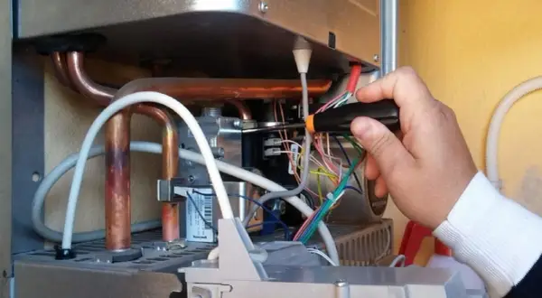 Tecnico effettua la pulizia della caldaia, lavorando sui cablaggi interni con un cacciavite.