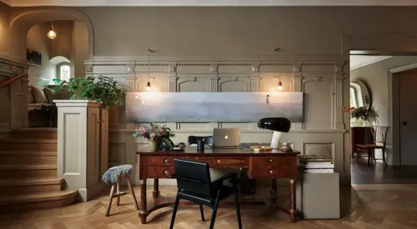Ett elegant skrivbord med laptop och lampa, i en hall med trappa och konst. Martin Brudnizki-inspirerad design.