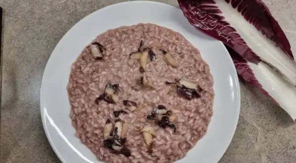 Un cremoso risotto al radicchio, con pezzetti di verdura che spuntano, accanto a una foglia fresca di radicchio.