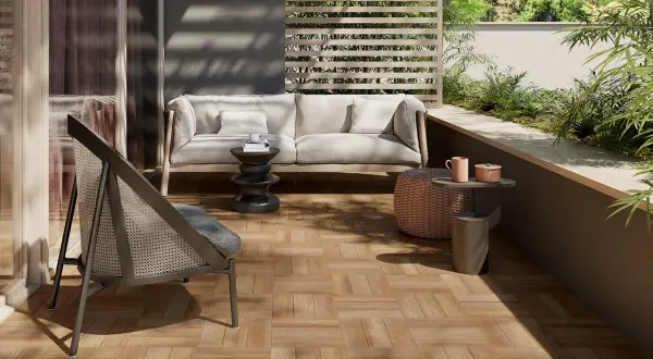 Terrazzo con pavimenti in gres porcellanato effetto legno, arredato con divano, poltrona e tavolini, immerso nel verde.